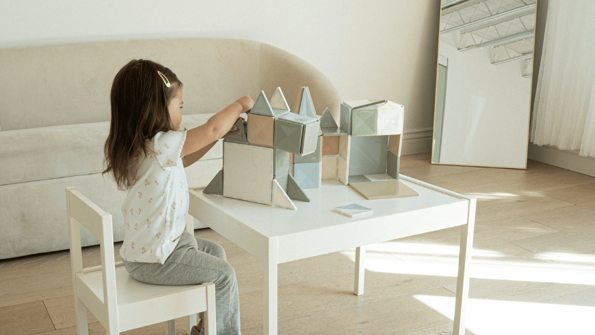 Toddler building a tall tower with neutral coconut milk magnetic tiles on a living room floor