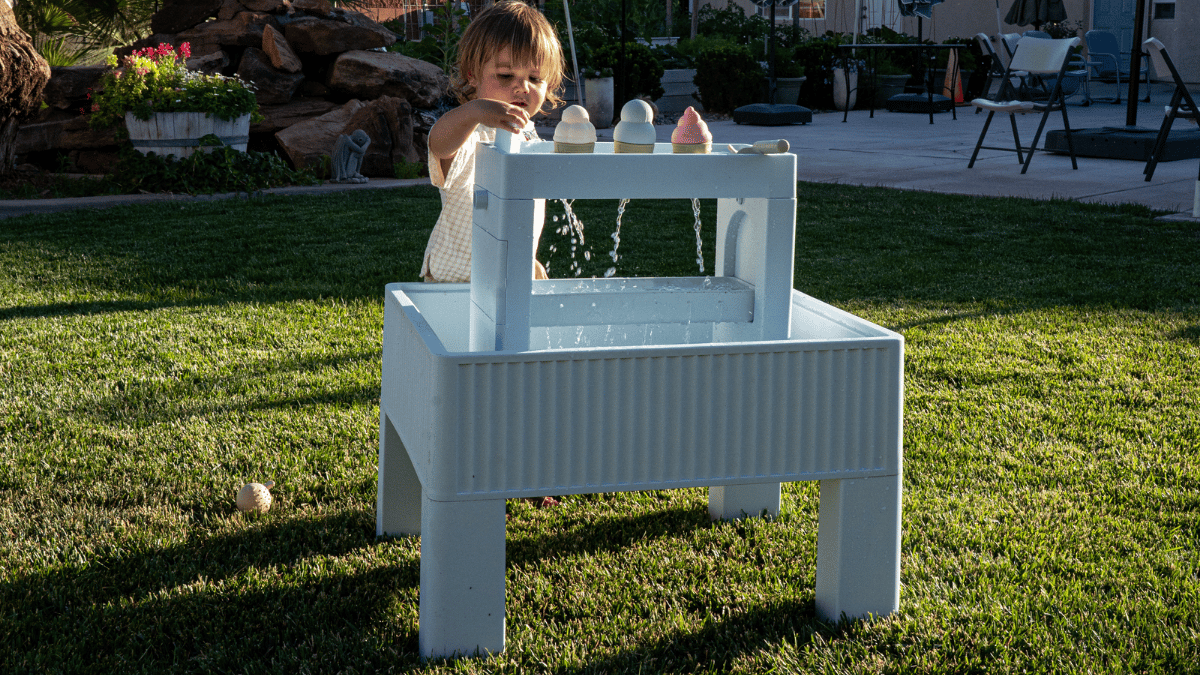 Modern water table for toddlers — toddler playing with the Splash & Play Table in backyard