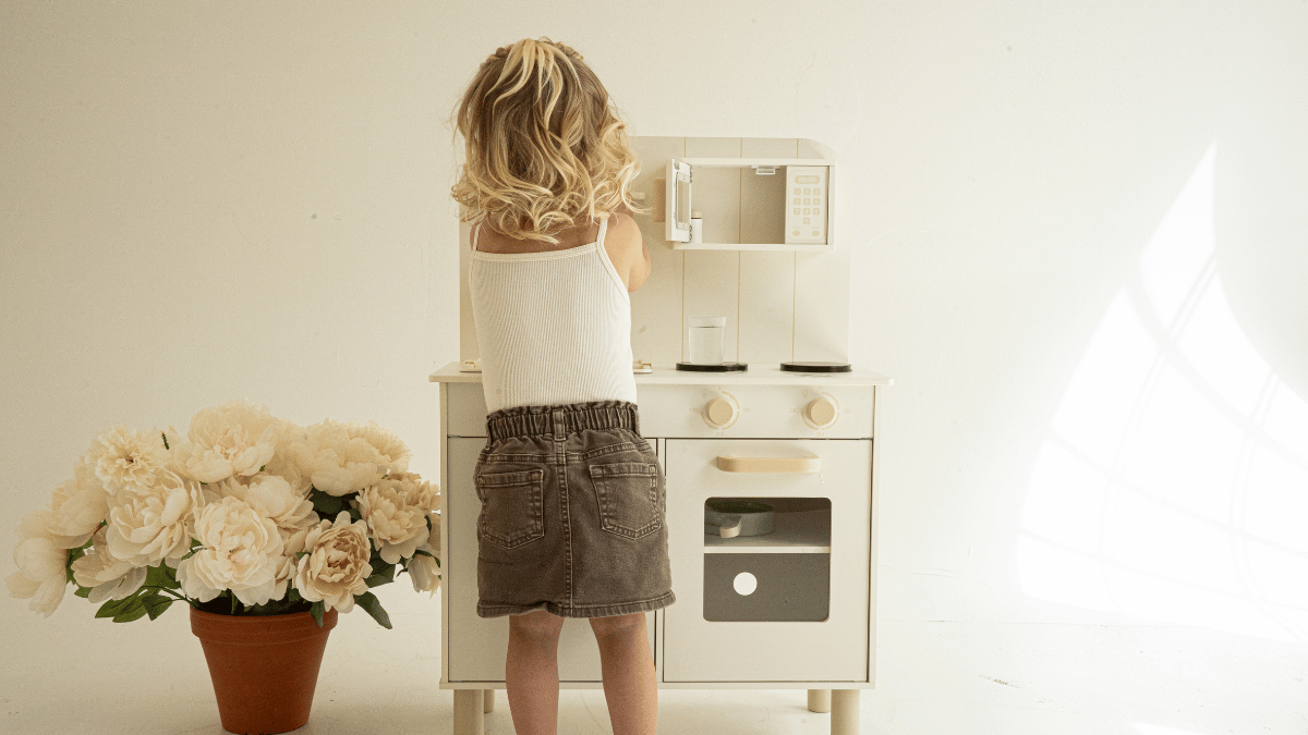 Toddler playing independently with play kitchen in a bright neutral playroom